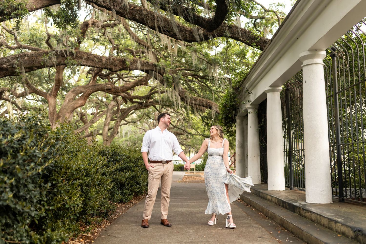 Couple holding hands while walking under a romantic pergola covered in blooming spring flowers and vines in a garden.