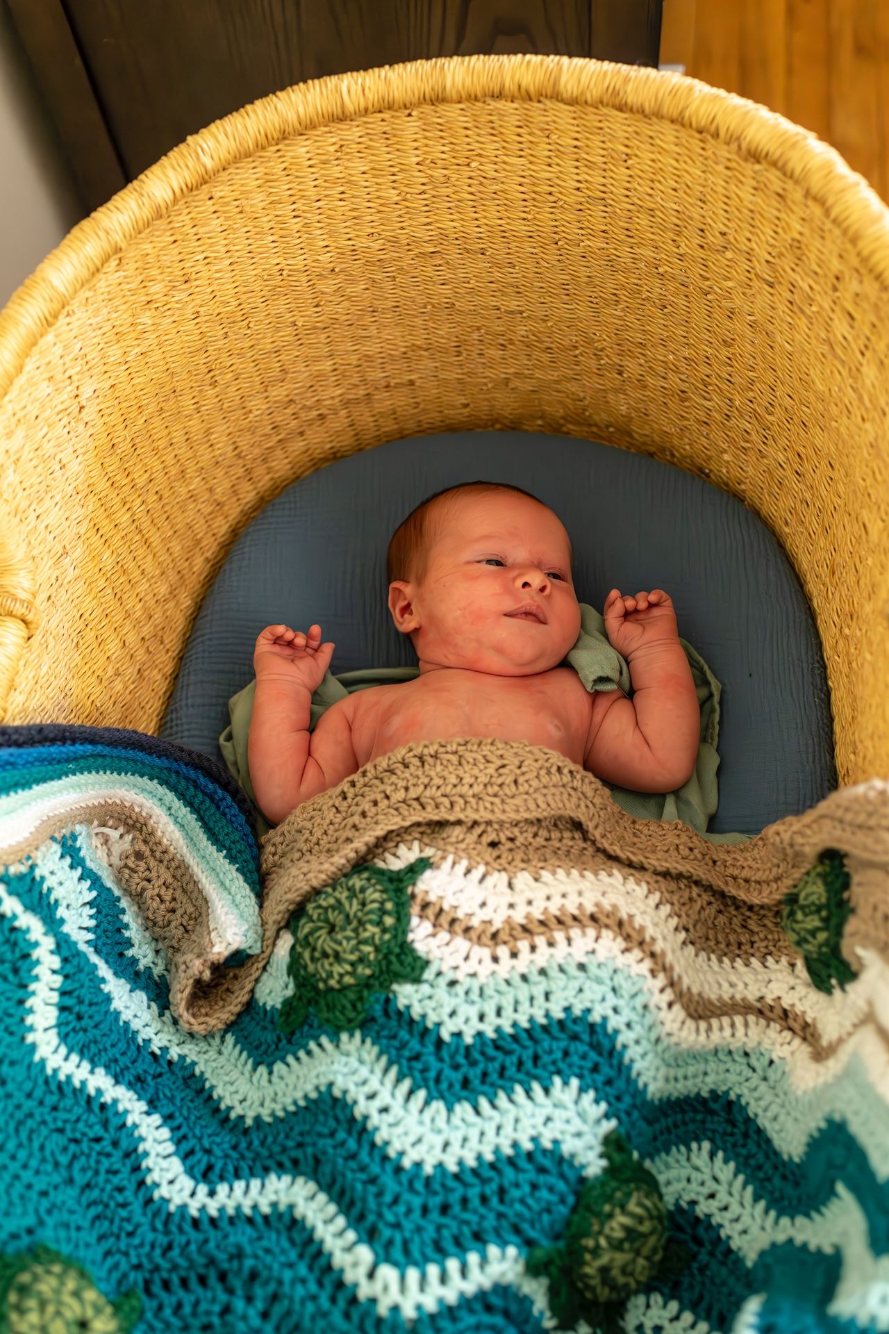 Baby rests on blue cushion covered with chevron-patterned blanket in teal and white crochet design.
