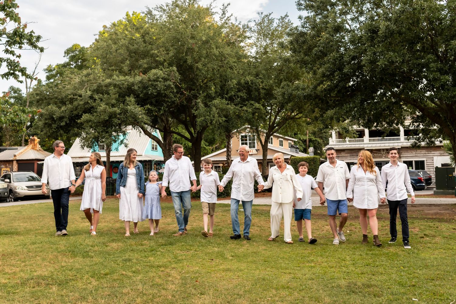 A group of people wearing white clothing hold hands while standing in a line on a grassy area near trees.