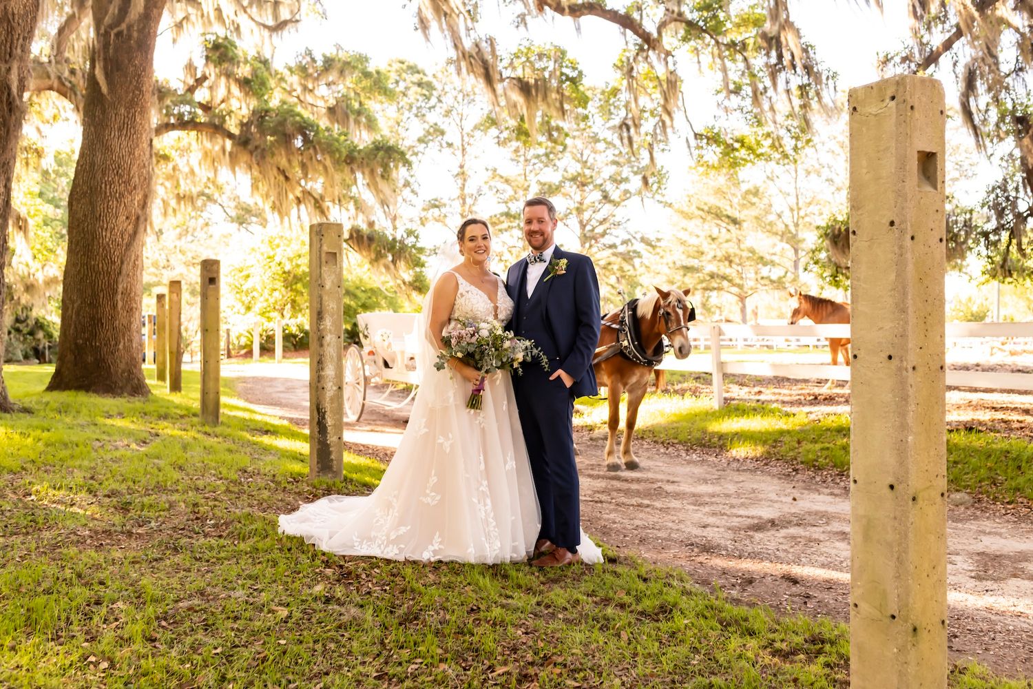 A couple stands outdoors among oak trees draped with Spanish moss during their sunset outdoor wedding ceremony.