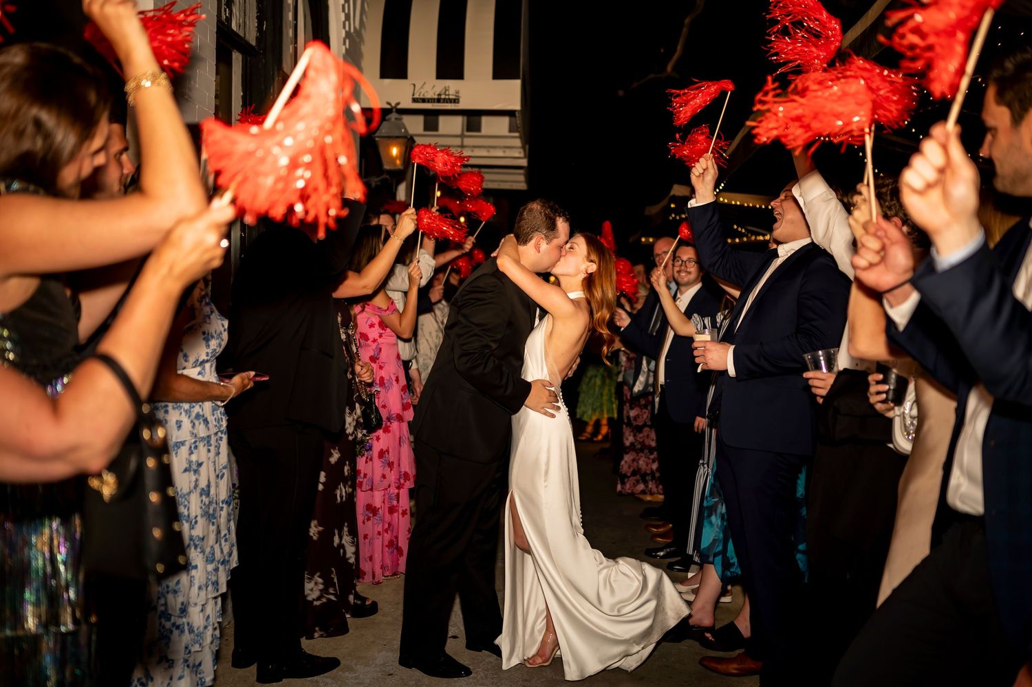 A couple shares a romantic dance at their wedding reception while guests celebrate with red pom poms and streamers.