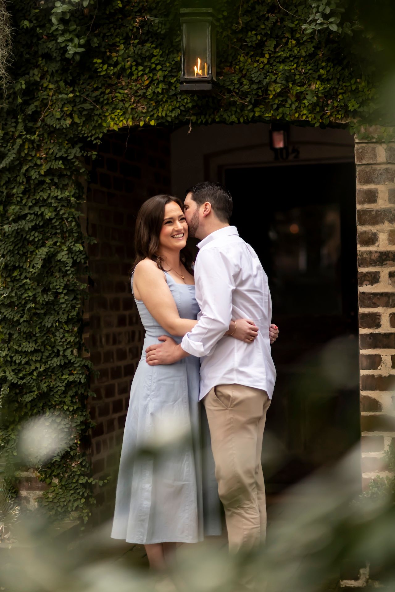Romantic couple embraces beneath ivy-covered brick archway with glowing lantern, creating an intimate garden atmosphere.