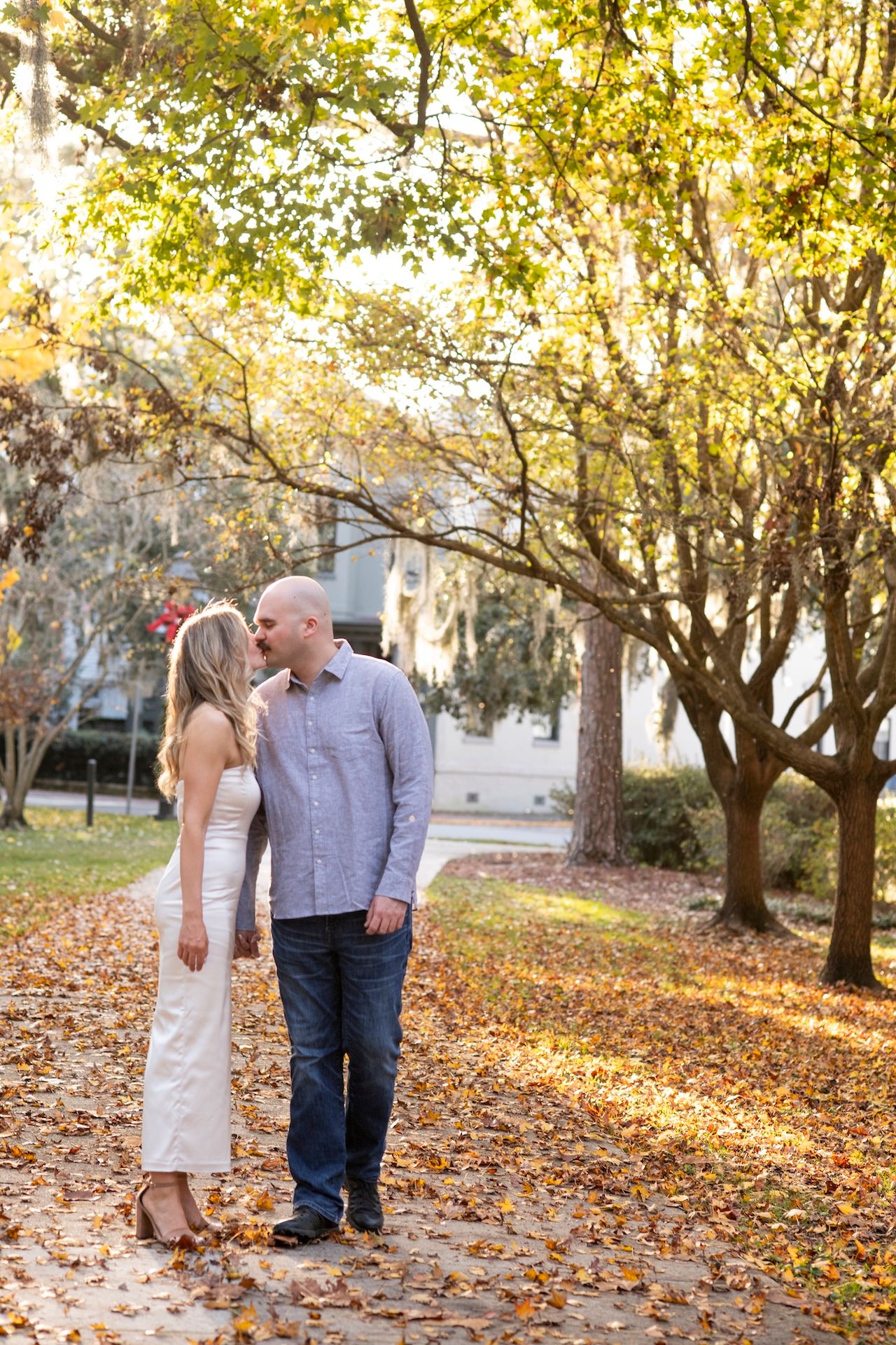 A couple shares tender moments surrounded by golden autumn leaves in a scenic park setting.