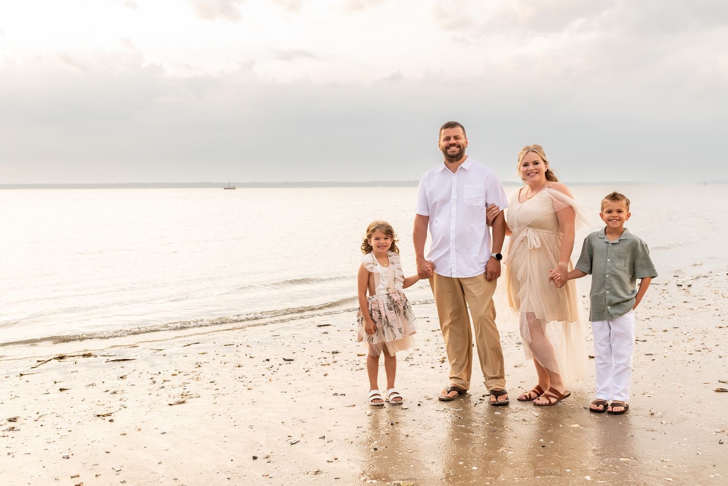 Family stands together on tranquil beach at sunset with ocean view and sandy shoreline.