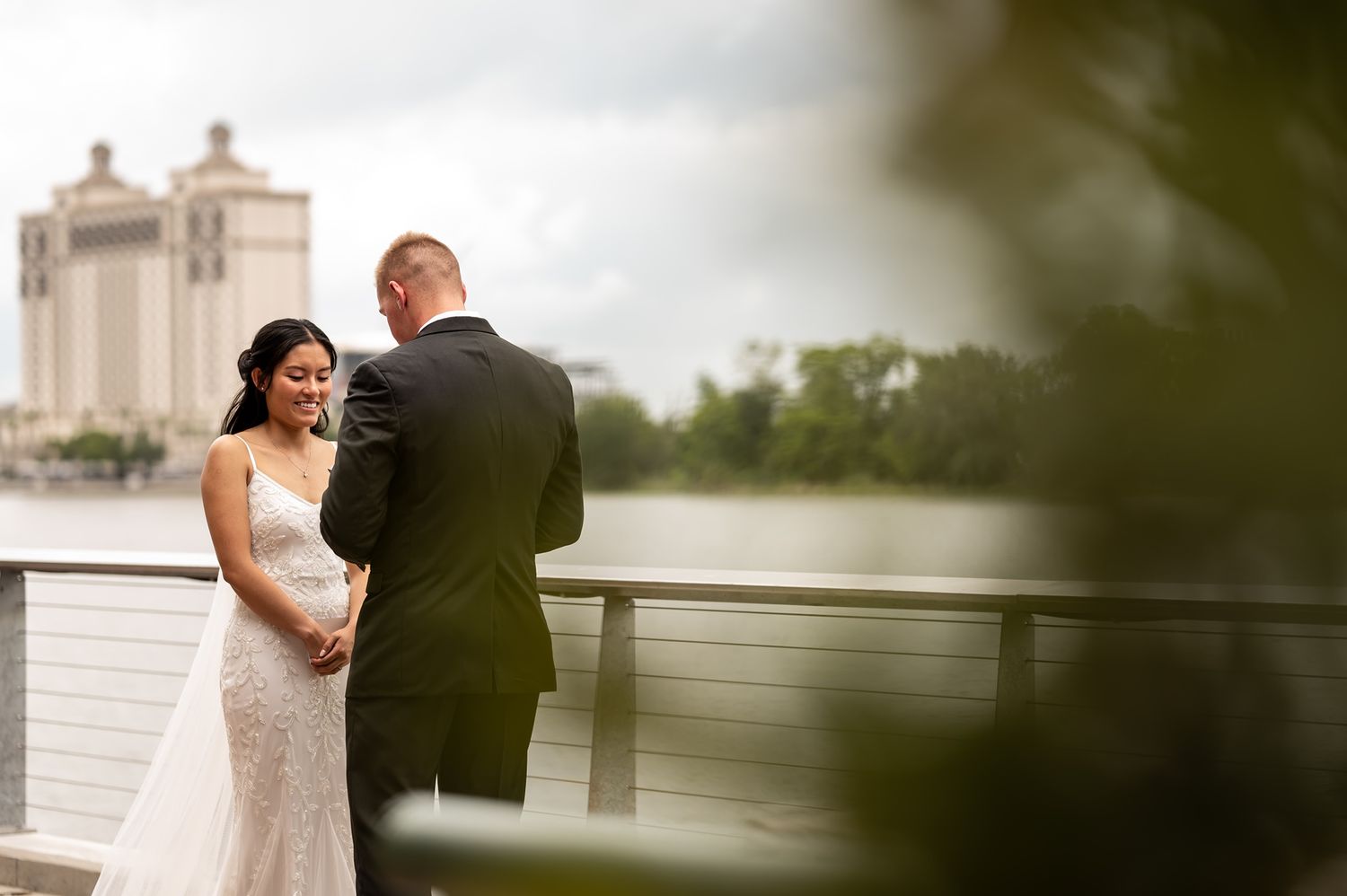 Newlywed couple stands intimately on deck overlooking industrial waterfront with grain silos in background.