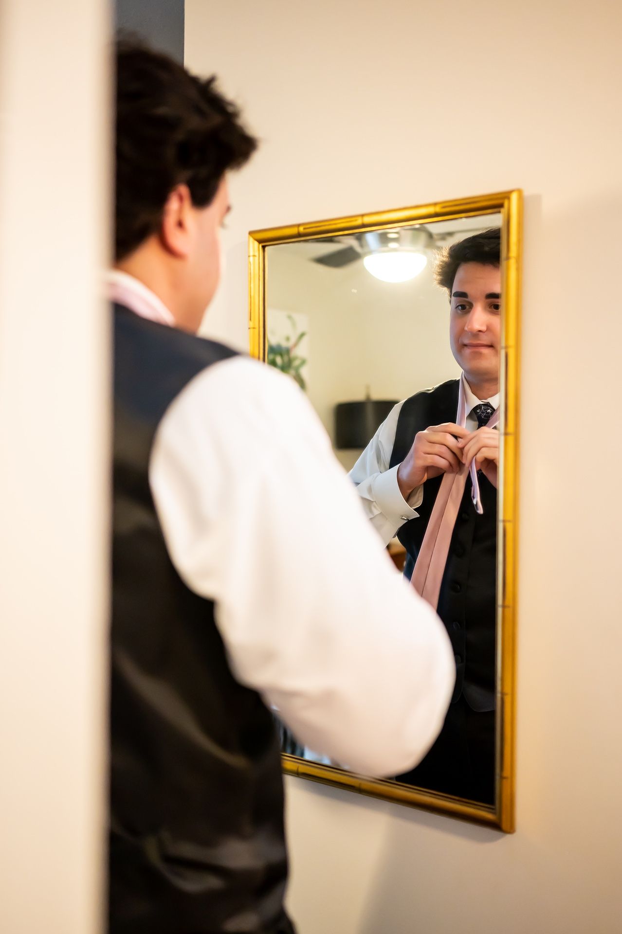 Person taking a self portrait photograph in a gold-framed mirror mounted on a beige wall.