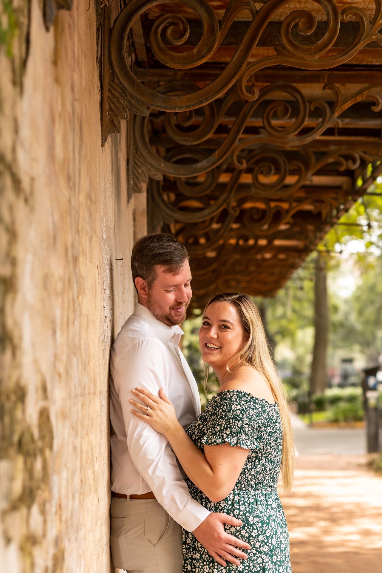 A couple shares tender embraces beneath ornate architectural details during their engagement photoshoot.