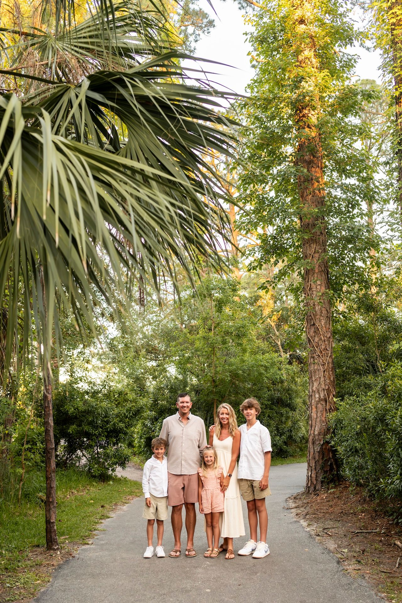 Family of five posing on a tree-lined path surrounded by palm trees and lush greenery.