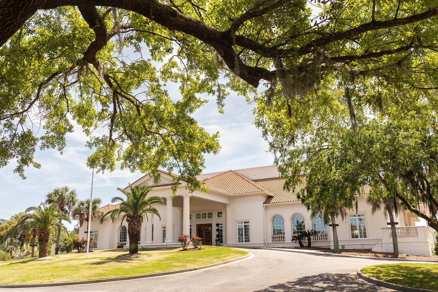 White church building with arched windows and columns set beneath large oak trees draped in Spanish moss.
