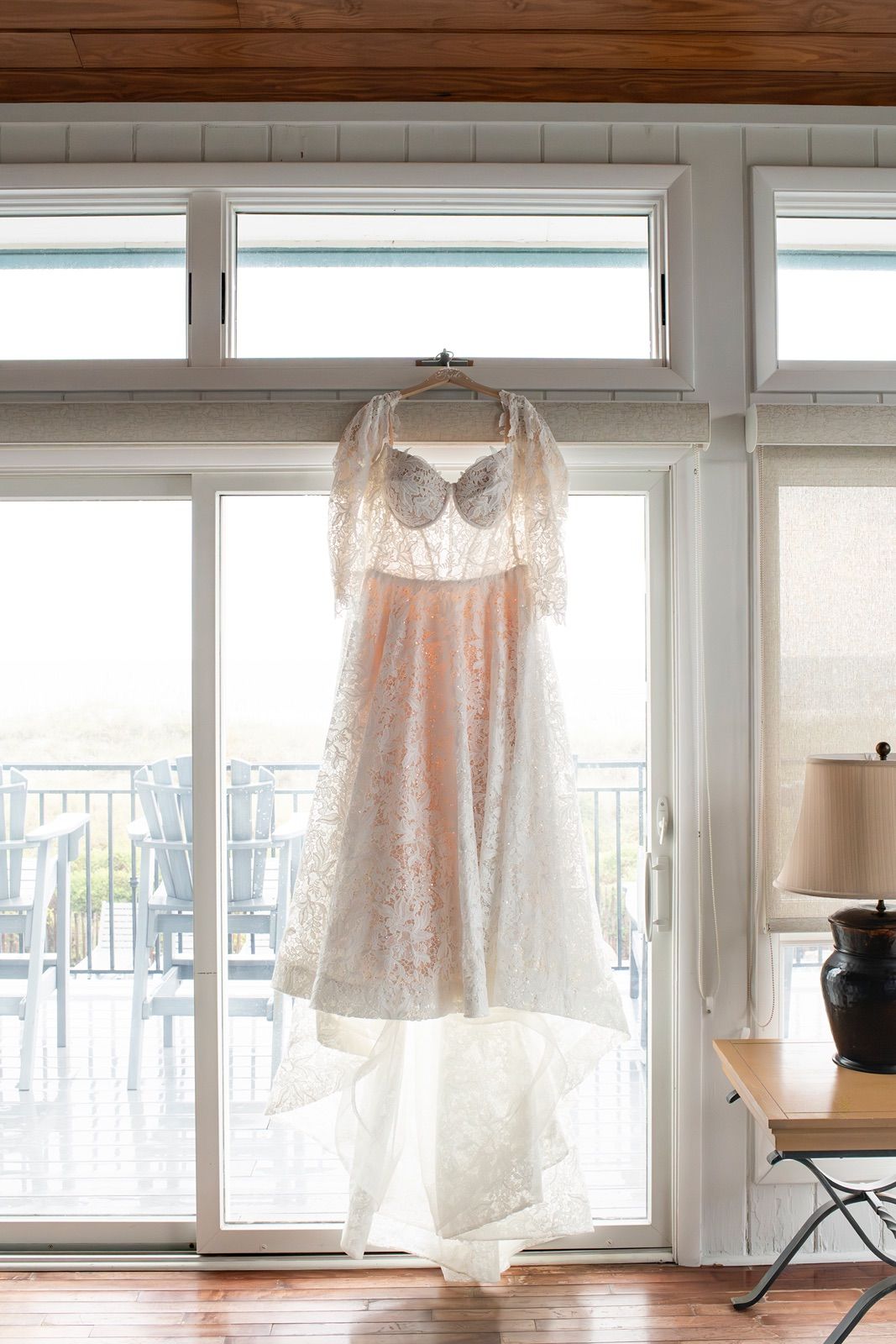 Five delicate lace wedding dresses hanging in sunlit windows create an ethereal bridal display.