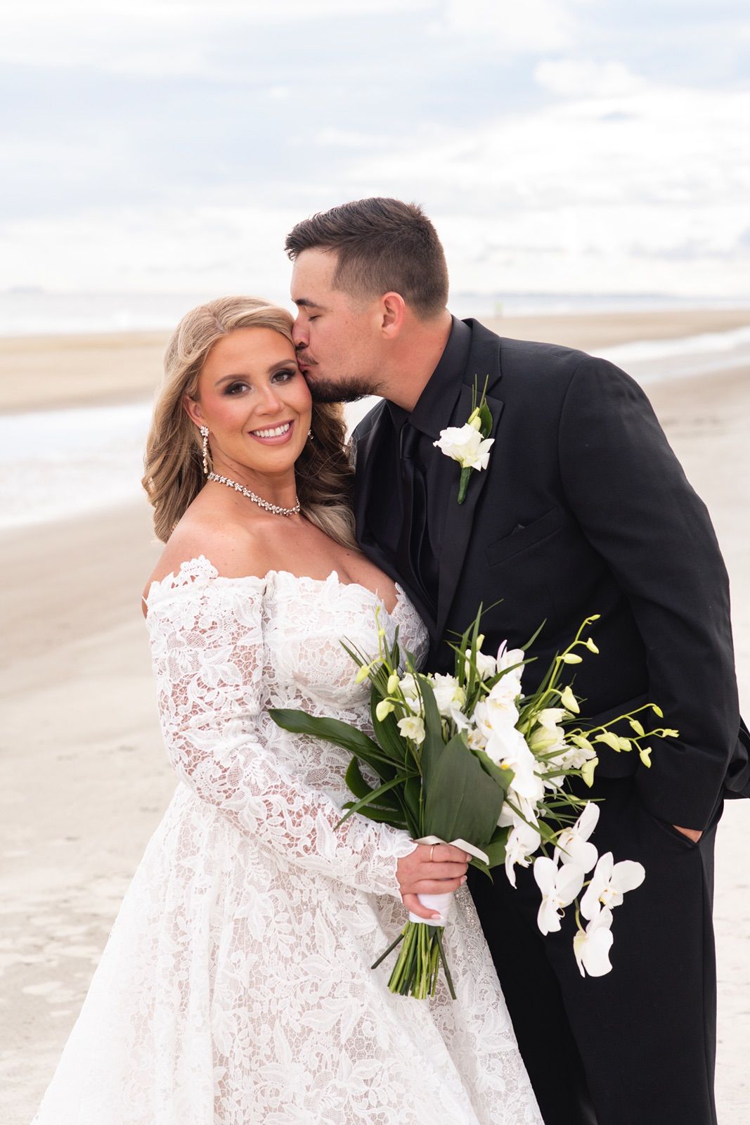 A romantic beach wedding scene with a couple in formal attire sharing intimate moments against a cloudy shoreline.
