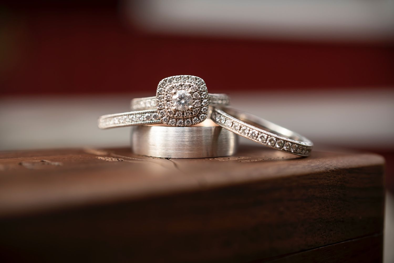 Diamond engagement ring and wedding bands arranged on brown wooden surface with elegant halo design and sparkling details.