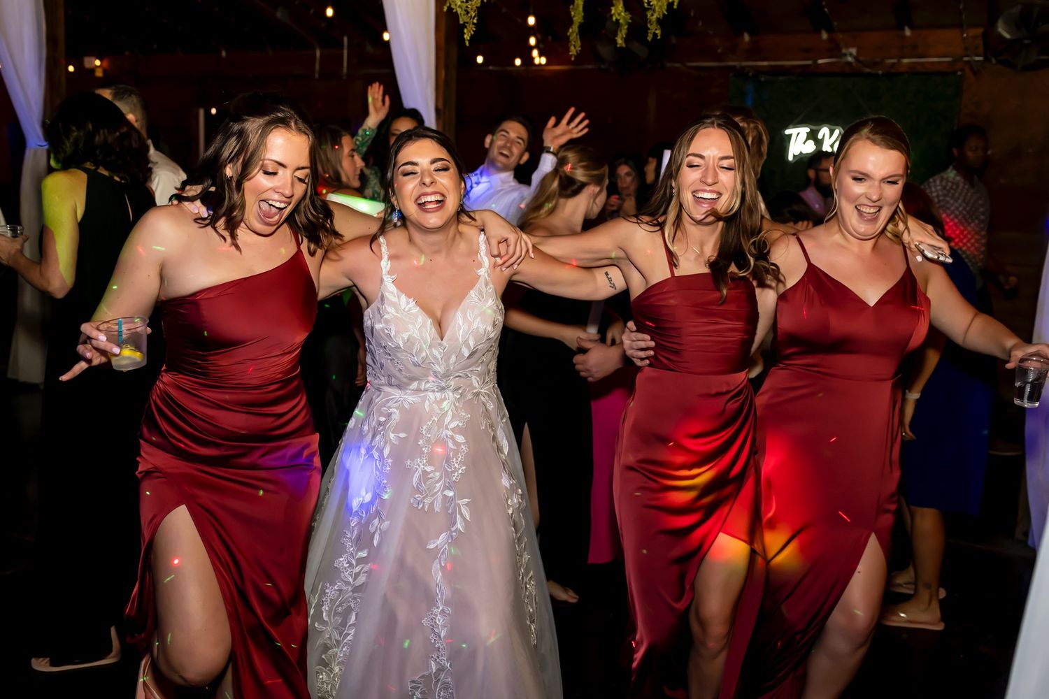 Wedding party members dance and celebrate joyfully together on the dance floor during the reception.