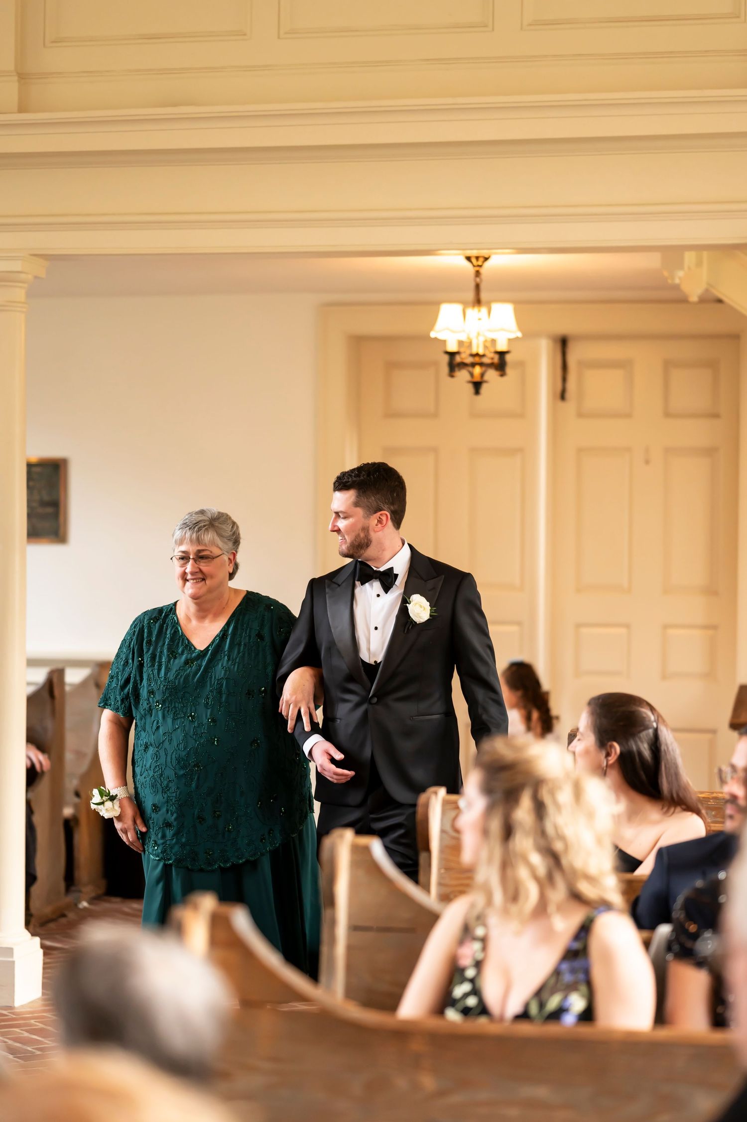 Wedding guests laughing and conversing during a formal reception in an elegant white paneled room.