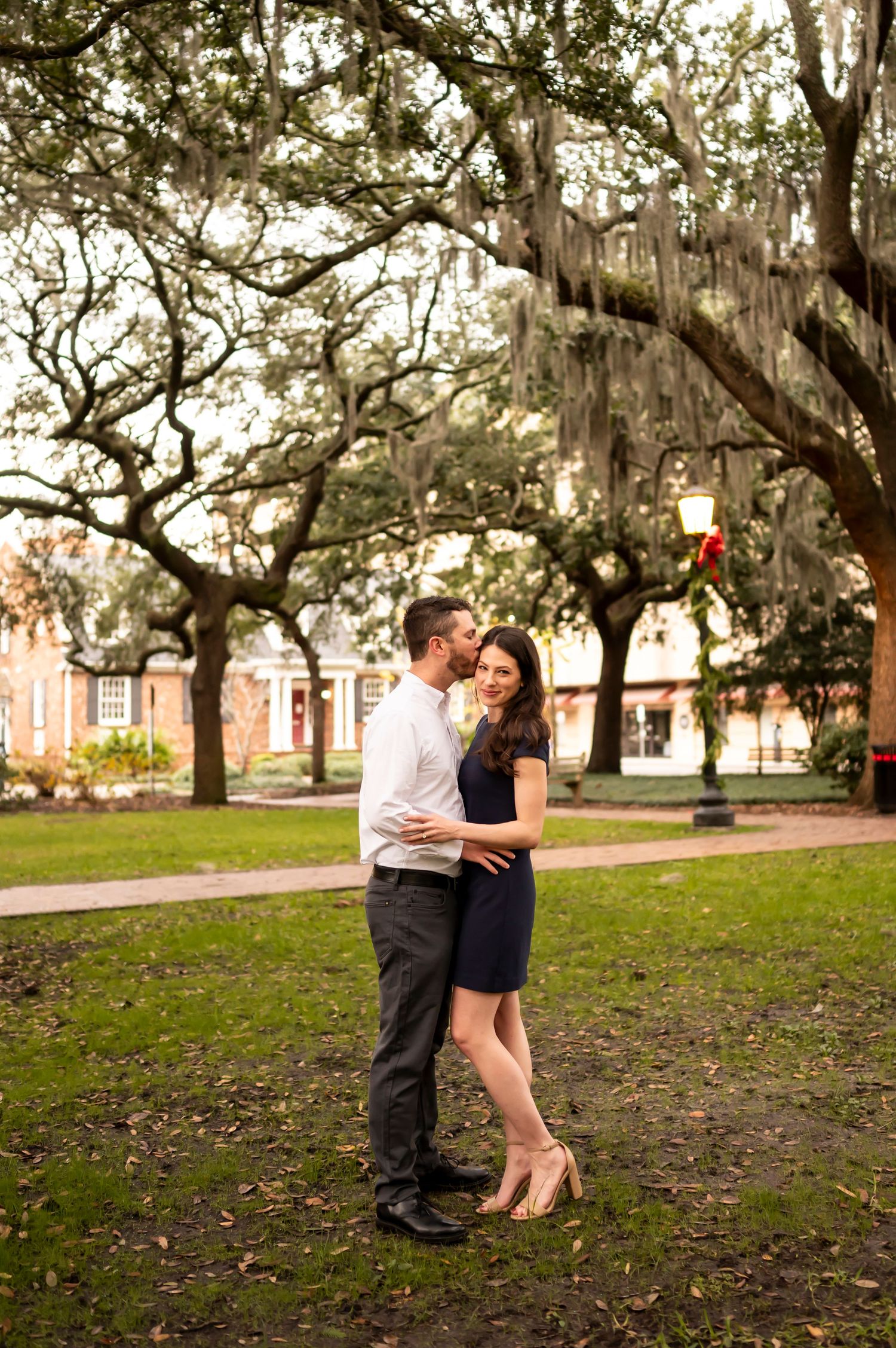 A romantic moment beneath Spanish moss draped oak trees in a peaceful Southern park setting.