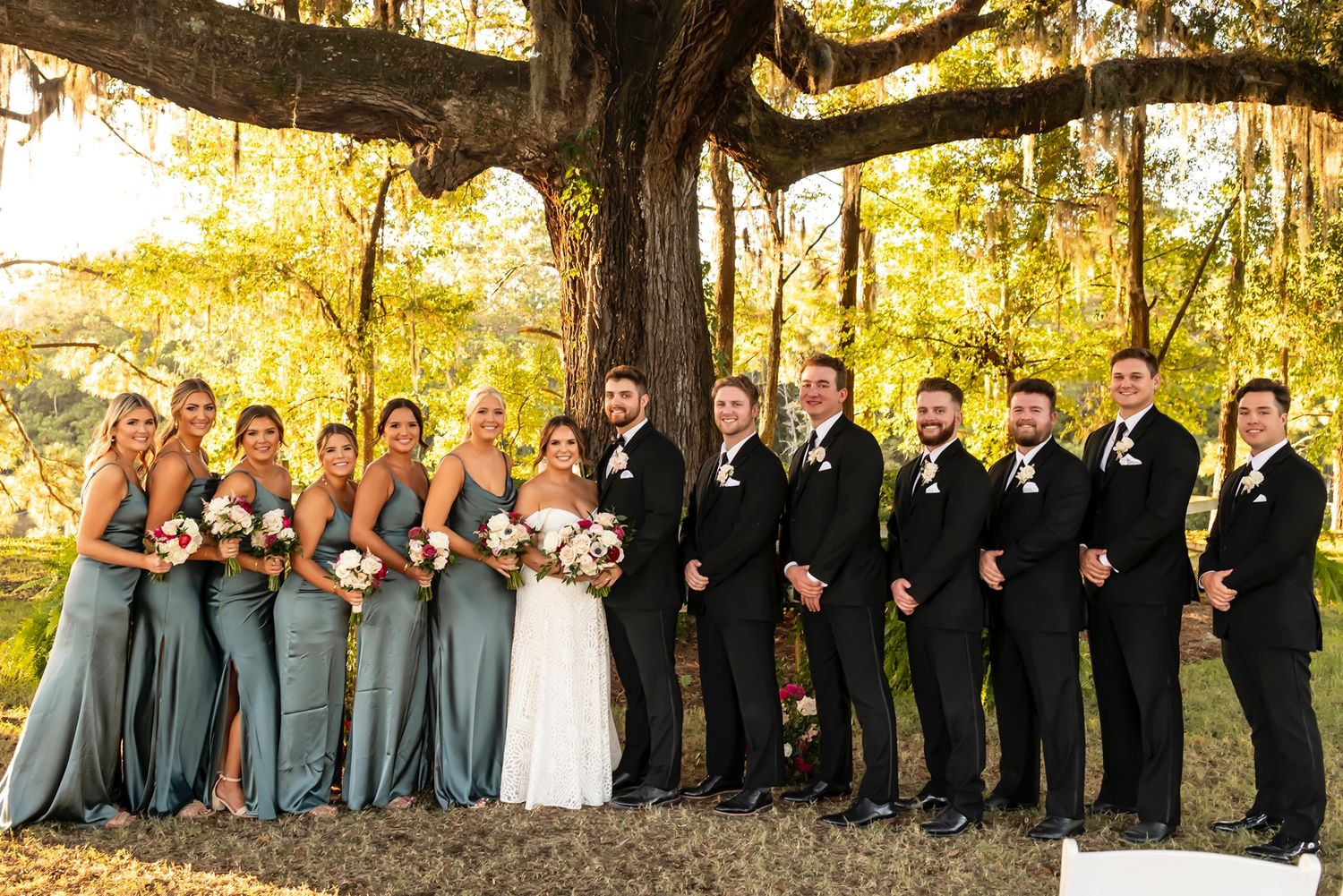 A wedding party poses together under golden autumn trees in coordinating gray and black formal attire.
