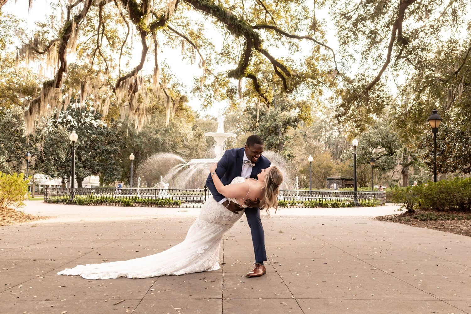 A romantic couple shares an intimate dip pose in front of a fountain at a garden venue during golden hour.