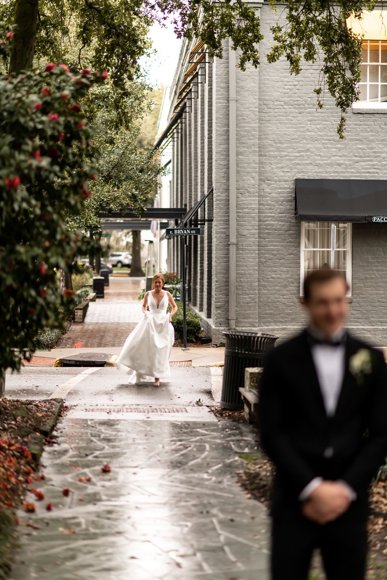 A wedding scene on a rainy brick sidewalk with greenery and white painted brick buildings in Charleston.