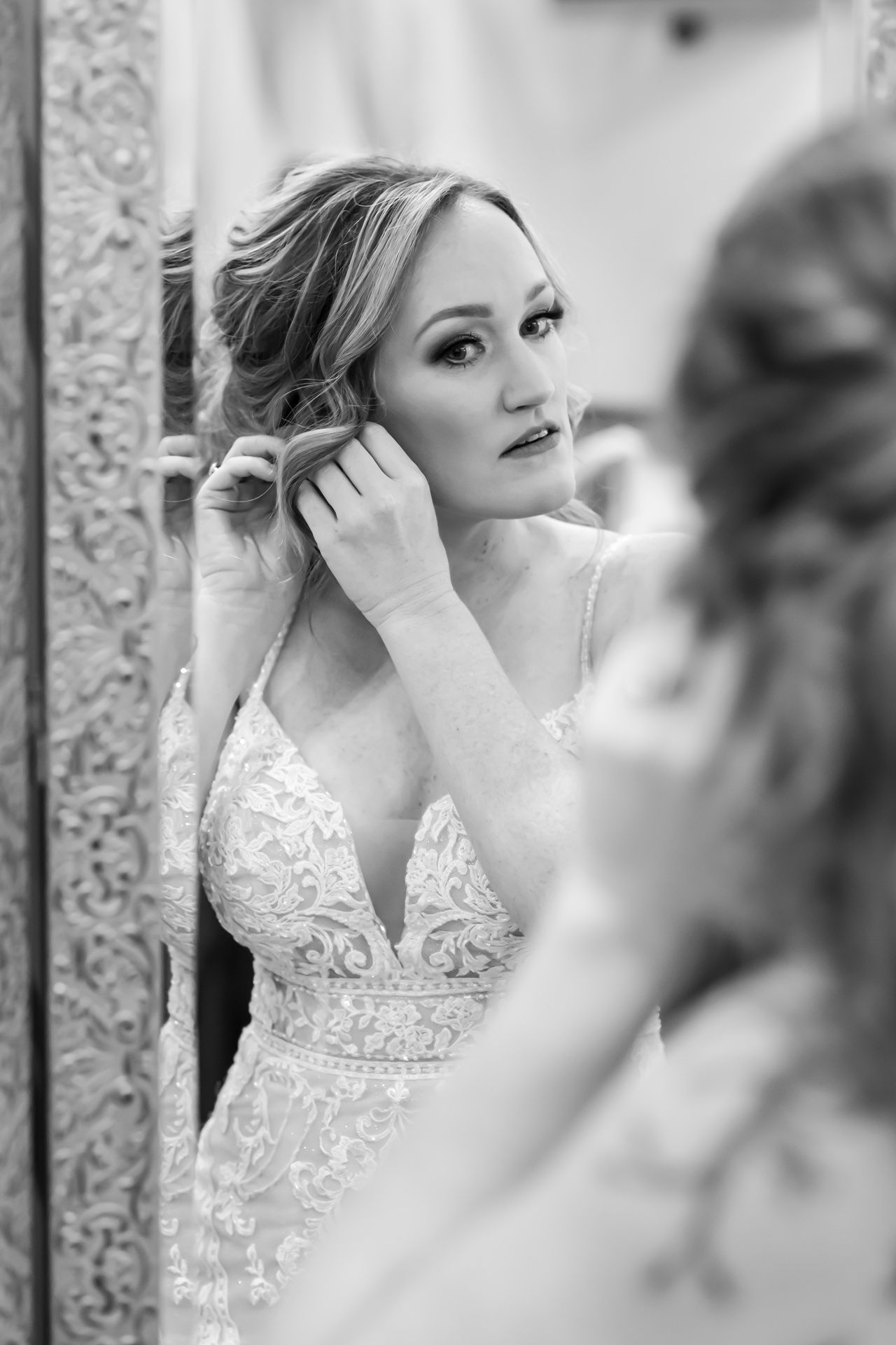 A black and white photo of someone wearing a delicate lace wedding gown with intricate embroidery details on top.