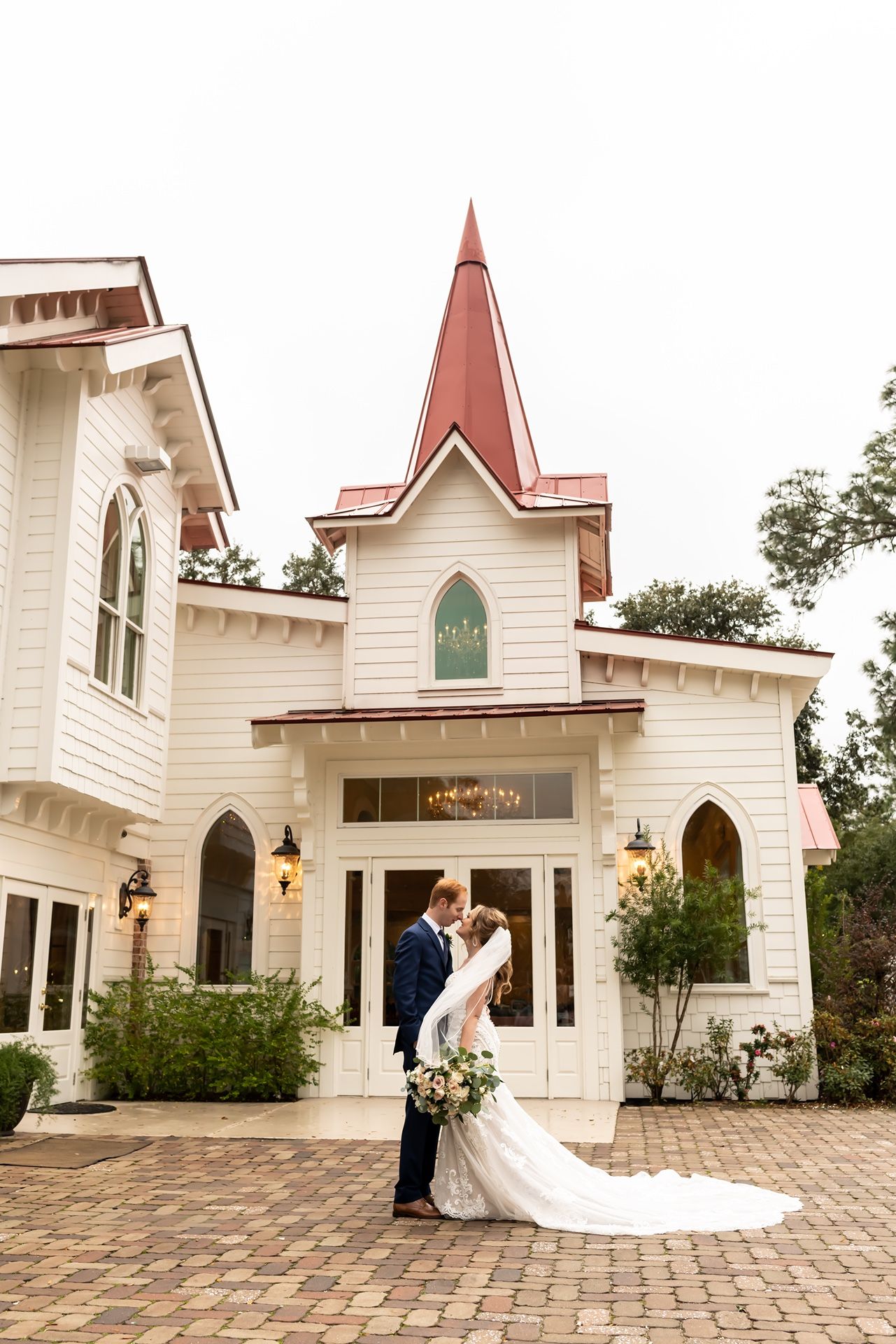 White chapel wedding venue with red roof and stone courtyard captured in panoramic view.