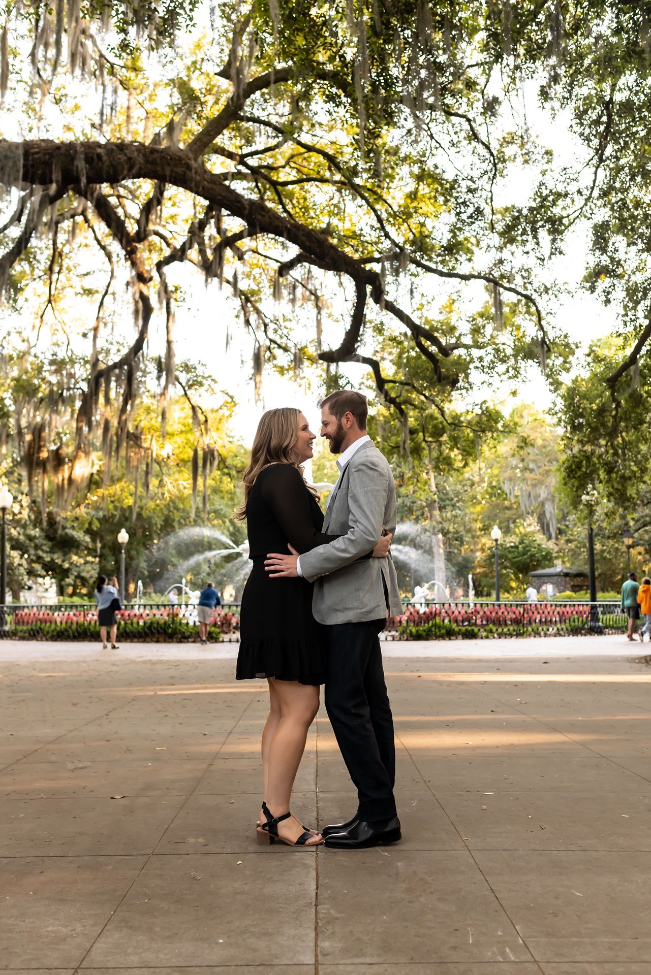 Couple embracing under Spanish moss draped oak trees in a romantic garden setting during golden hour.