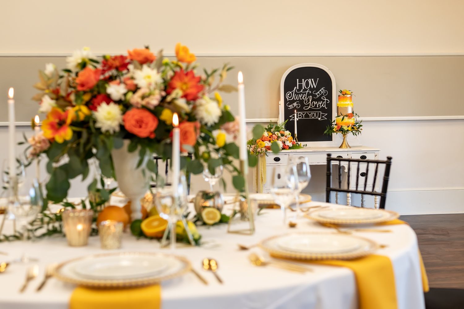 Elegant table setting with floral centerpiece, gold chargers, and chalkboard sign at reception venue.