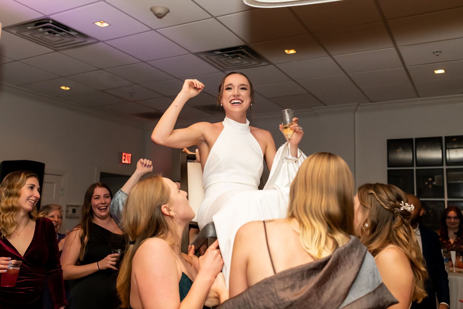 A group of people dancing and celebrating at a lively indoor party with overhead lighting.