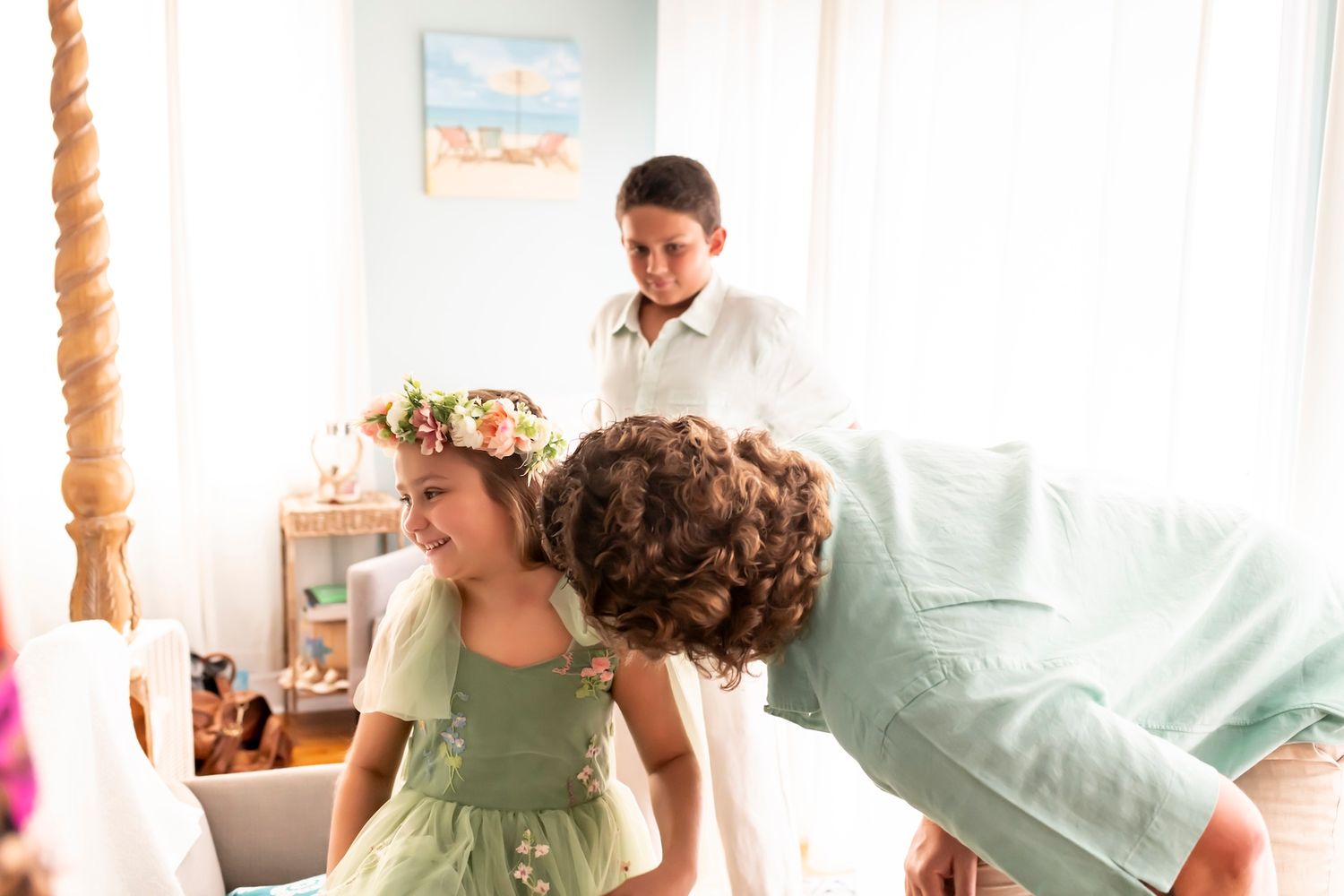 People in a bright sunlit room enjoying an intimate gathering with flowers and a painted beach scene on the wall.