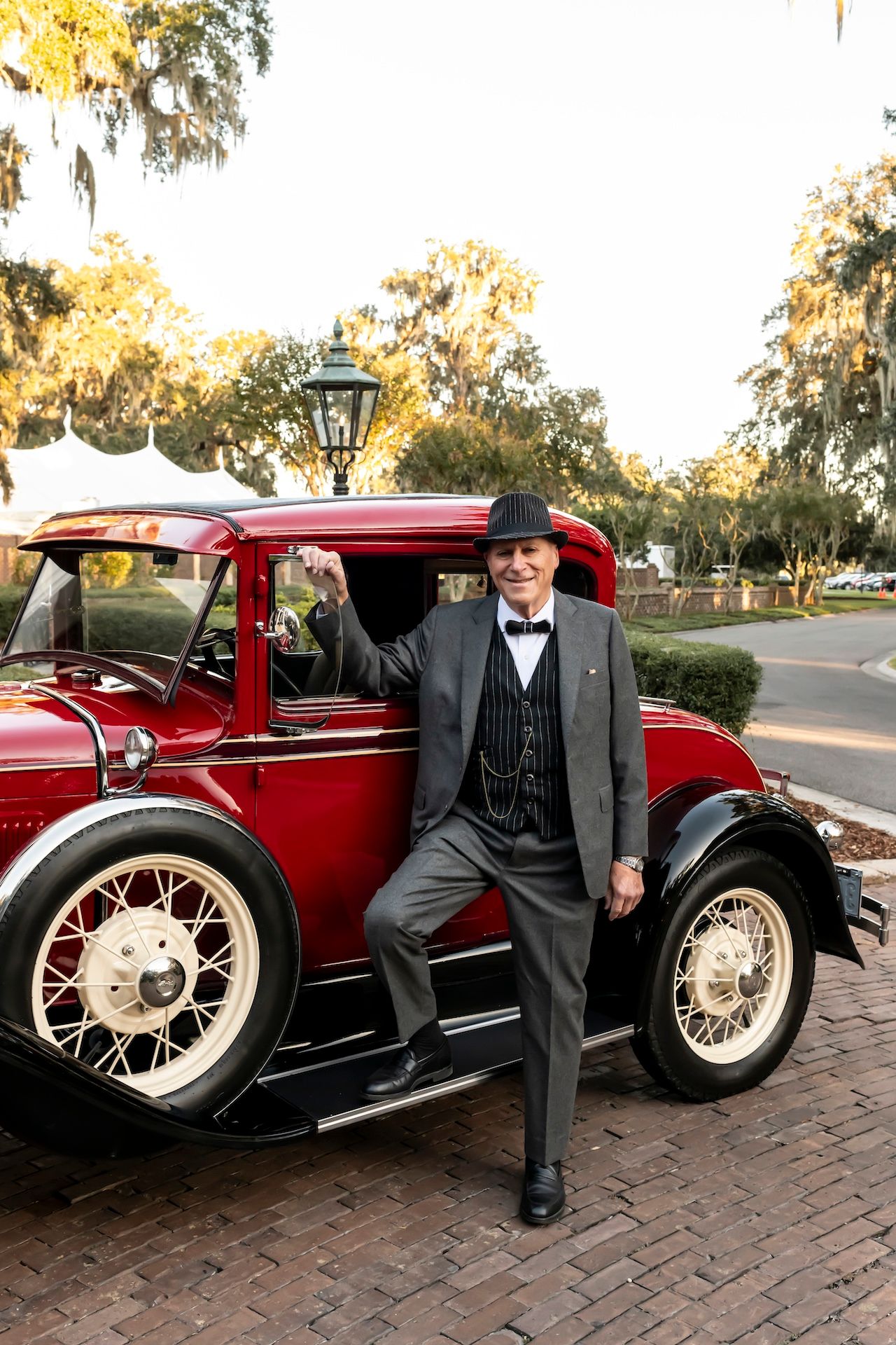 A vintage red Ford Model A car parked on brick pavement with Spanish moss draped trees in the background.