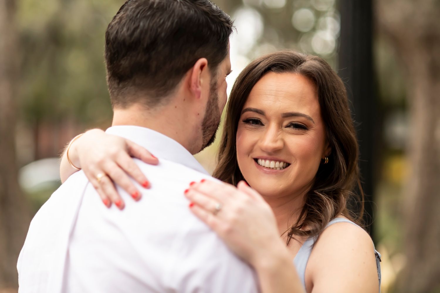A romantic outdoor portrait shows an intimate moment between two people embracing in soft natural lighting.