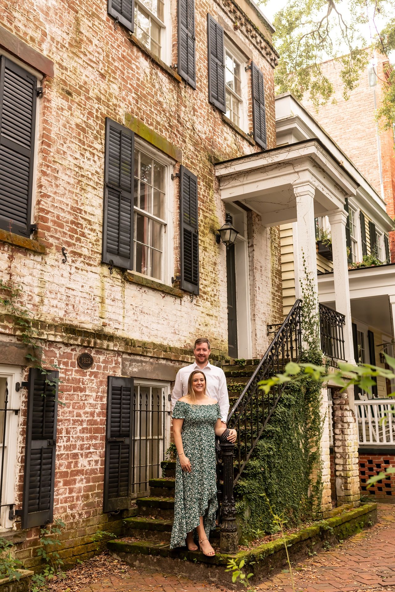 Historic red brick building with black shutters and white columns along a charming walkway in autumn.