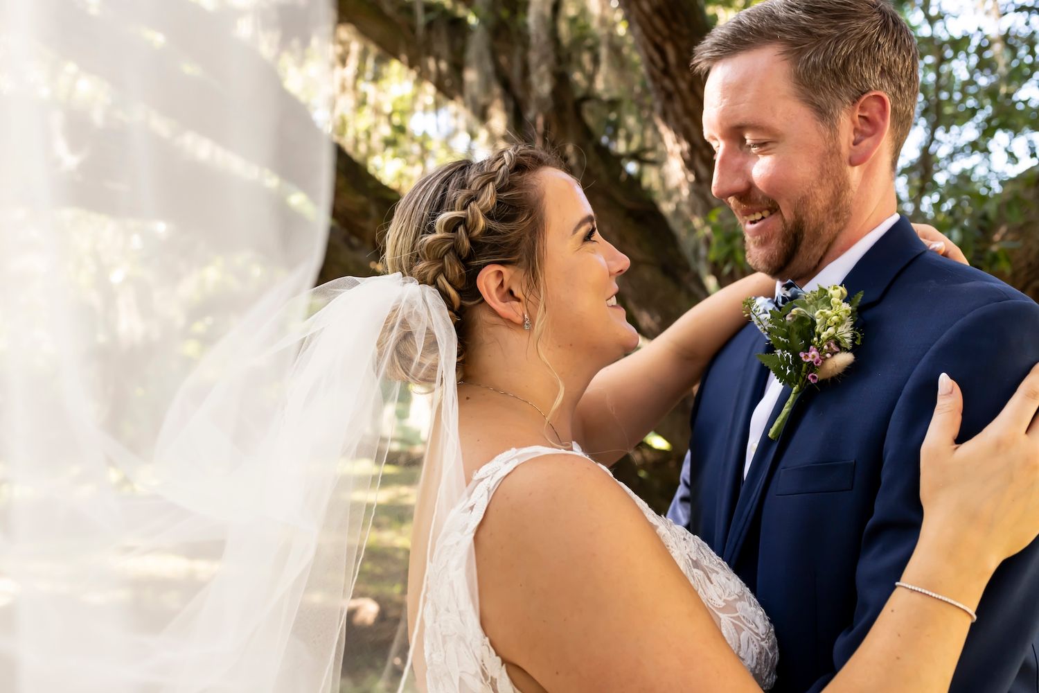 A joyful couple shares an intimate moment on their wedding day with the bride wearing a white veil and groom in navy suit.