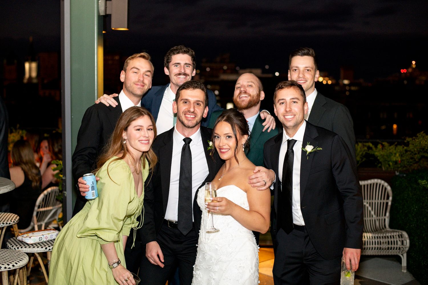 Wedding party members in formal attire pose together outdoors at night during a celebration.