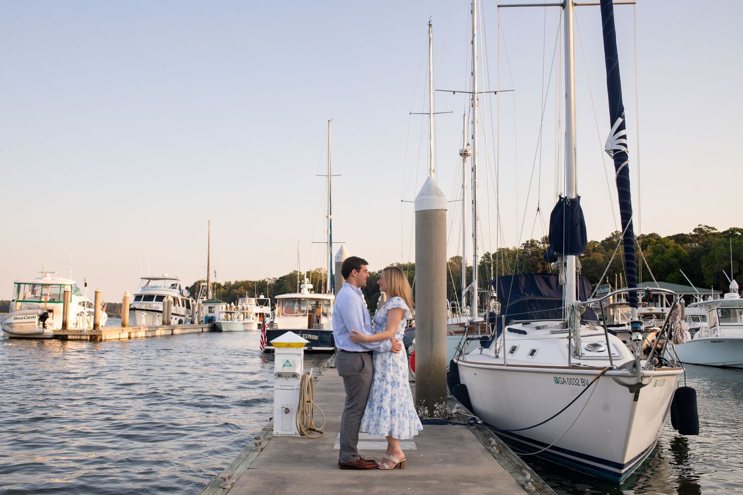 Sailboats docked at a marina during sunset with calm waters and clear skies in the background.