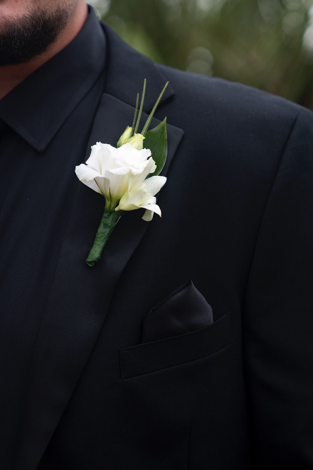 Close-up detail shots of white floral boutonnieres on black suit lapels at a formal event.