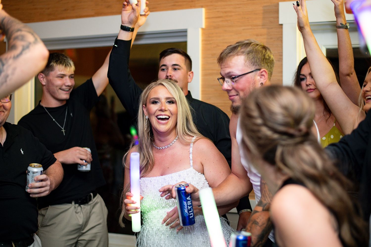 Wedding celebration with guests dancing and holding glowing party favors on a dance floor.