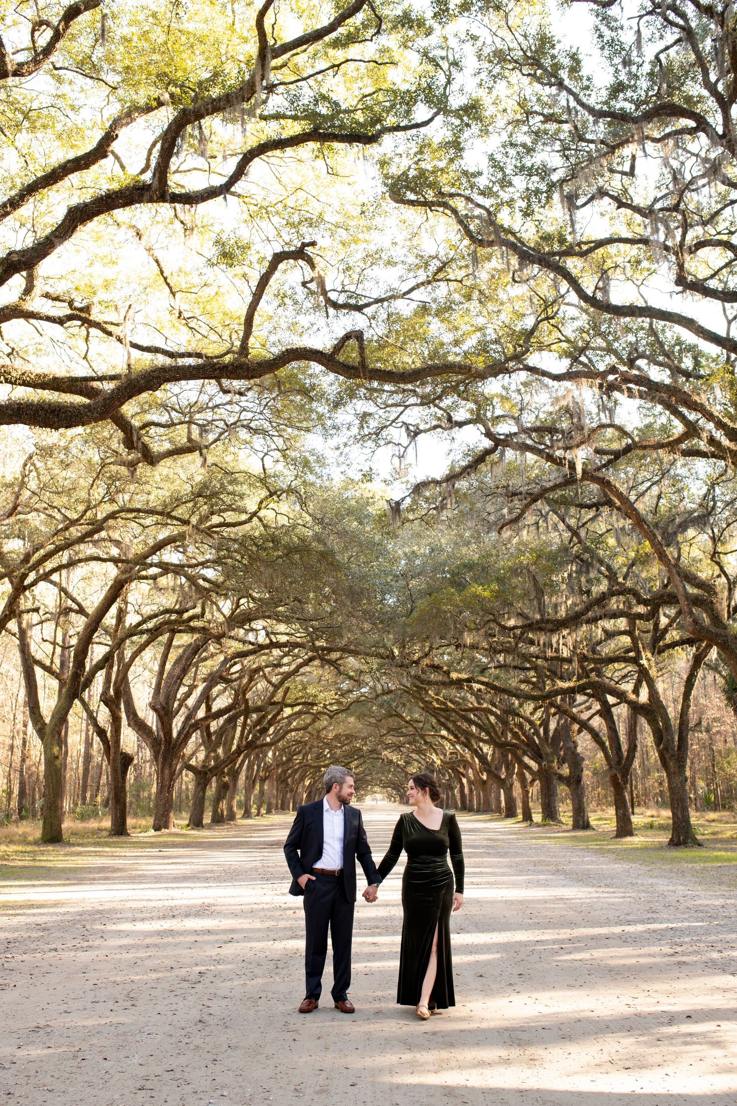 Couple holding hands walking down a tree-lined path at Wormsloe Historic Site in Savannah, Georgia.