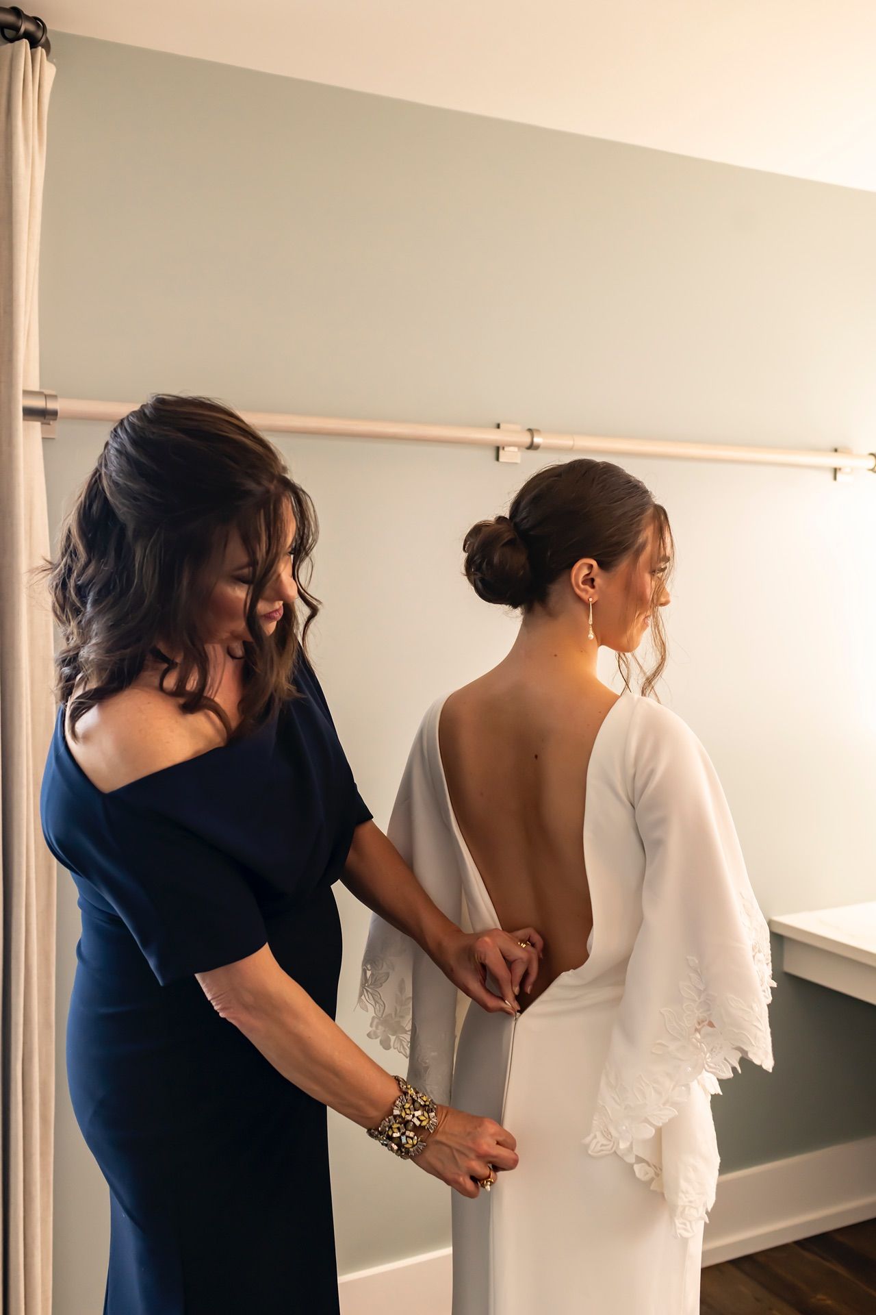 Two people helping someone prepare for a wedding in a bright white dressing room.