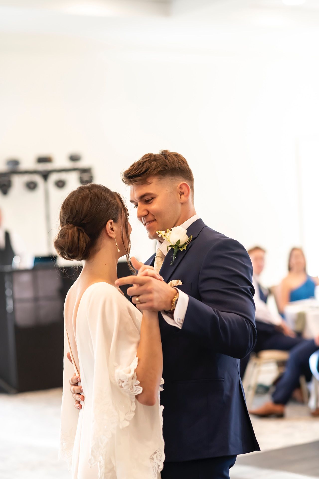 A couple shares their first dance at their wedding reception, with the bride in white and groom in navy suit.