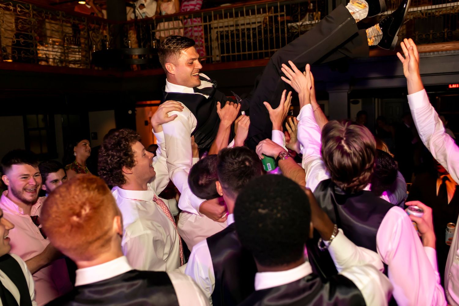 Energetic crowd celebrating at wedding reception venue with hands raised.