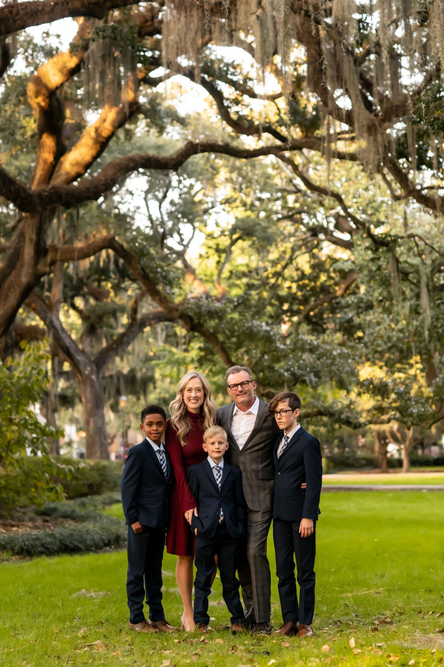 A family portrait beneath towering oak trees draped with Spanish moss in a park setting.