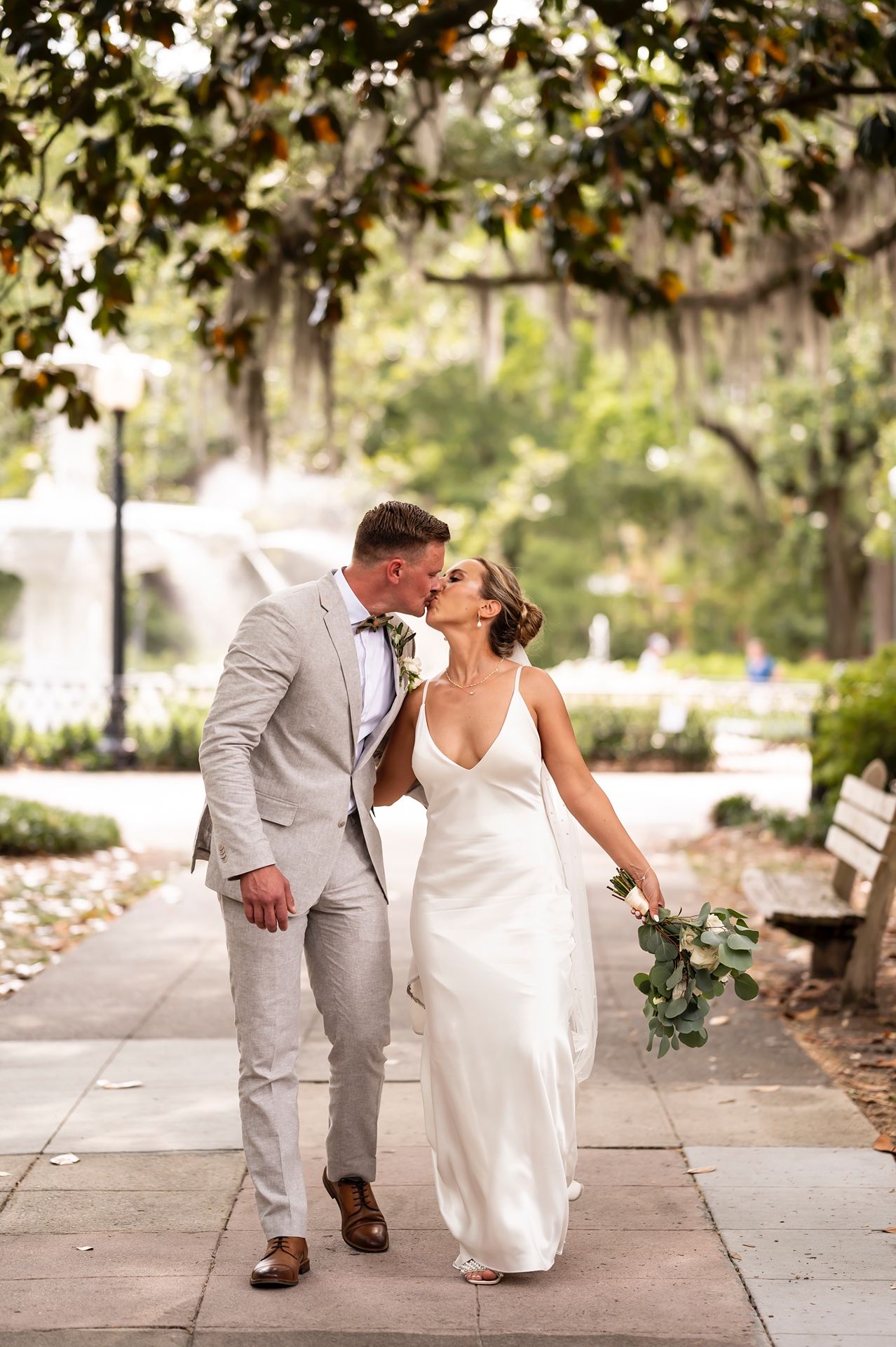 Newlywed couple sharing a romantic moment while walking under moss-draped trees in a Southern garden setting.