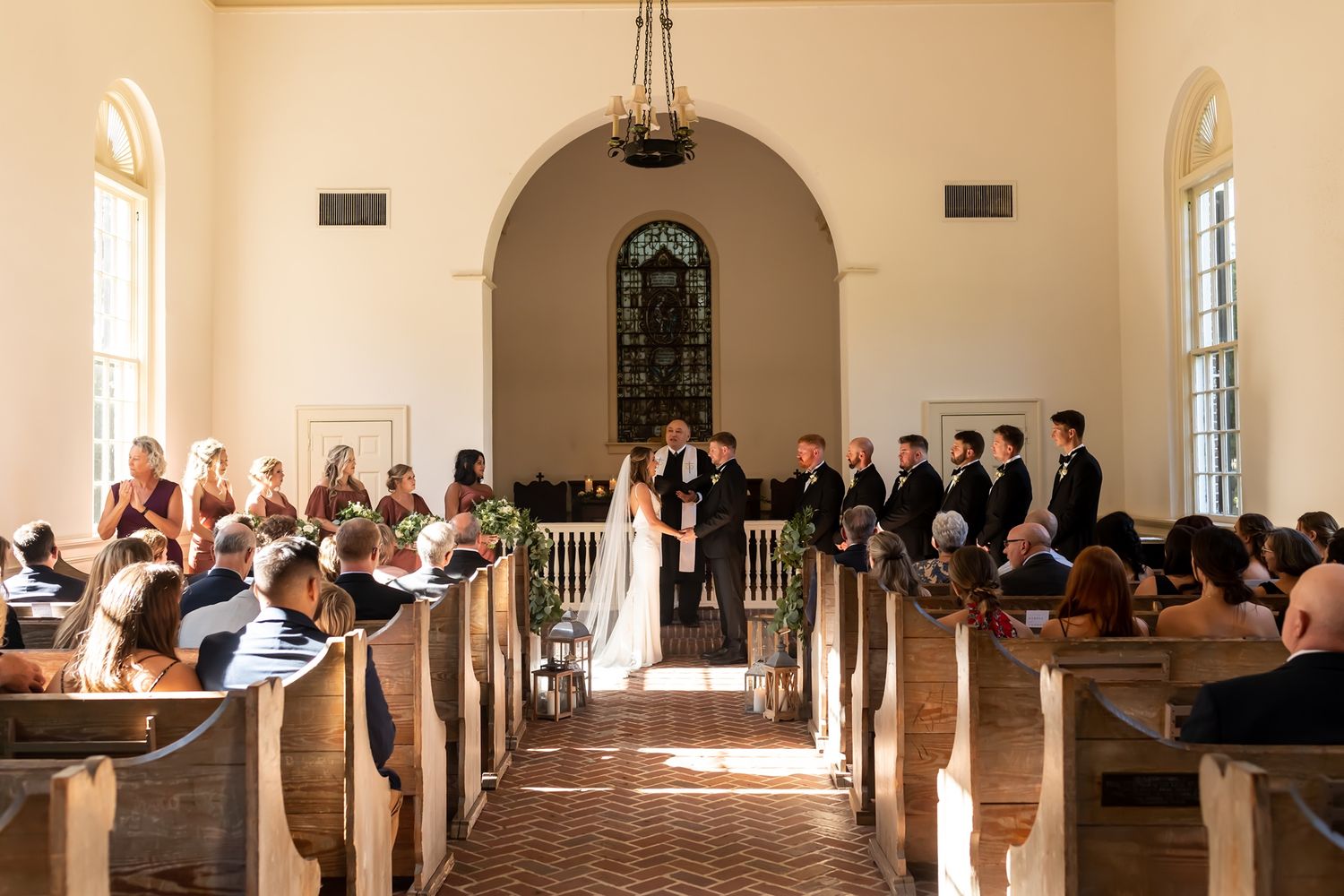 Guests seated in wooden church pews inside a bright chapel with arched windows and natural light streaming through.