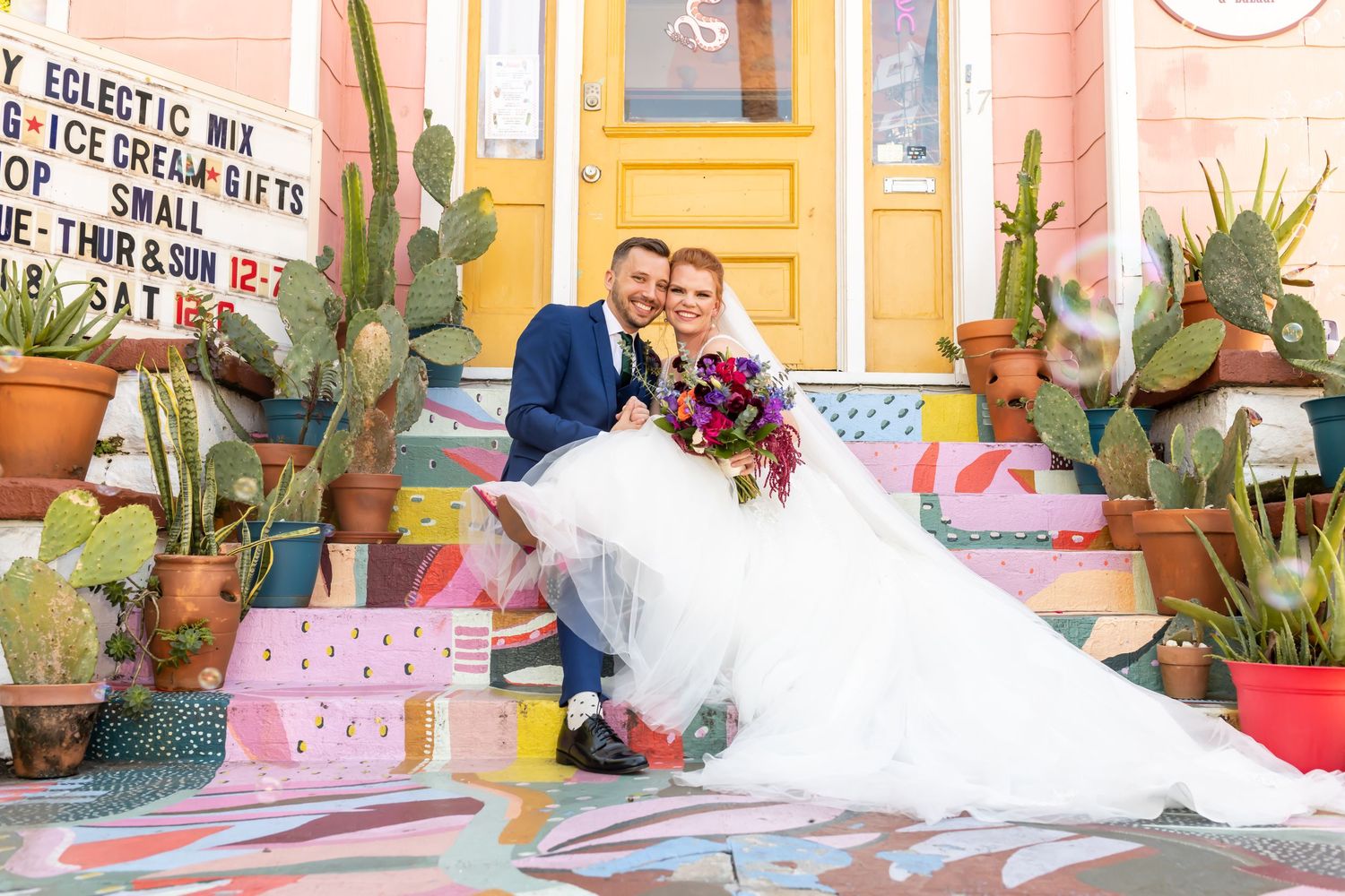 Bride and groom in front of colorful shop.
