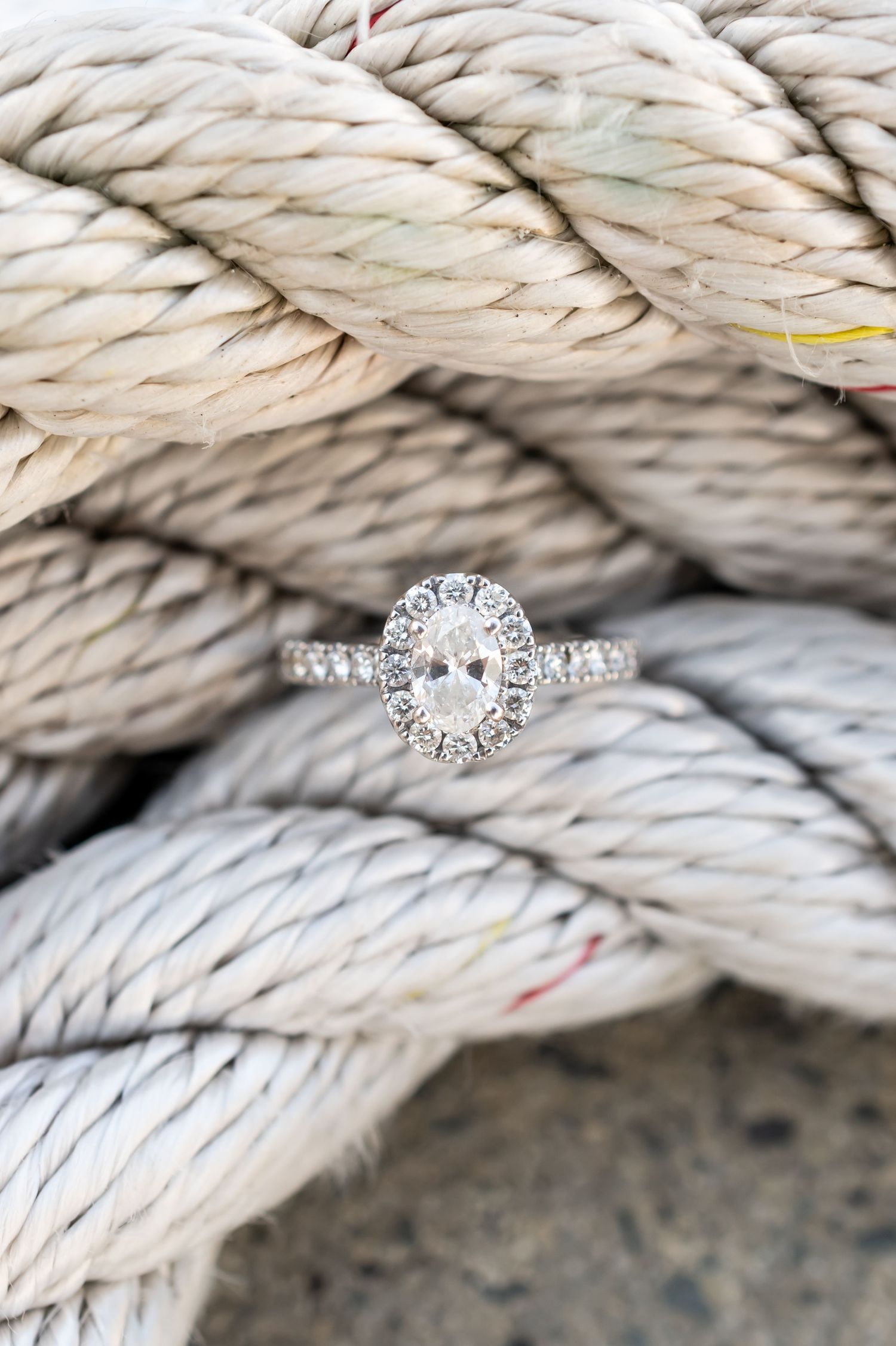 Elegant oval diamond engagement ring with pave band resting on coiled nautical rope.