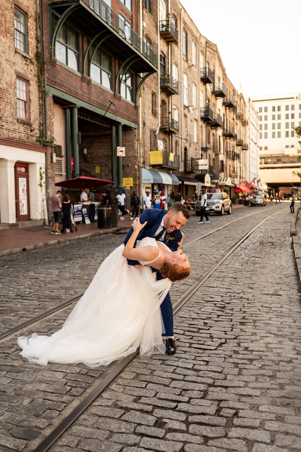 Newlywed couple dips romantically on historic cobblestone street with brick buildings in the background.