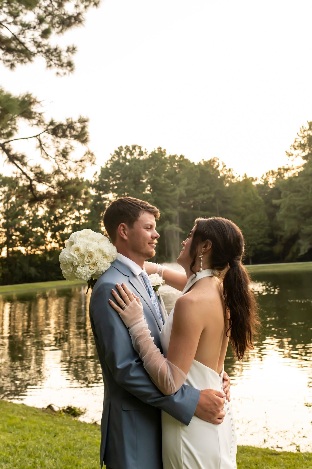 A tender moment between newlyweds embracing by a tranquil lake at sunset, creating a romantic silhouette against the golden light.