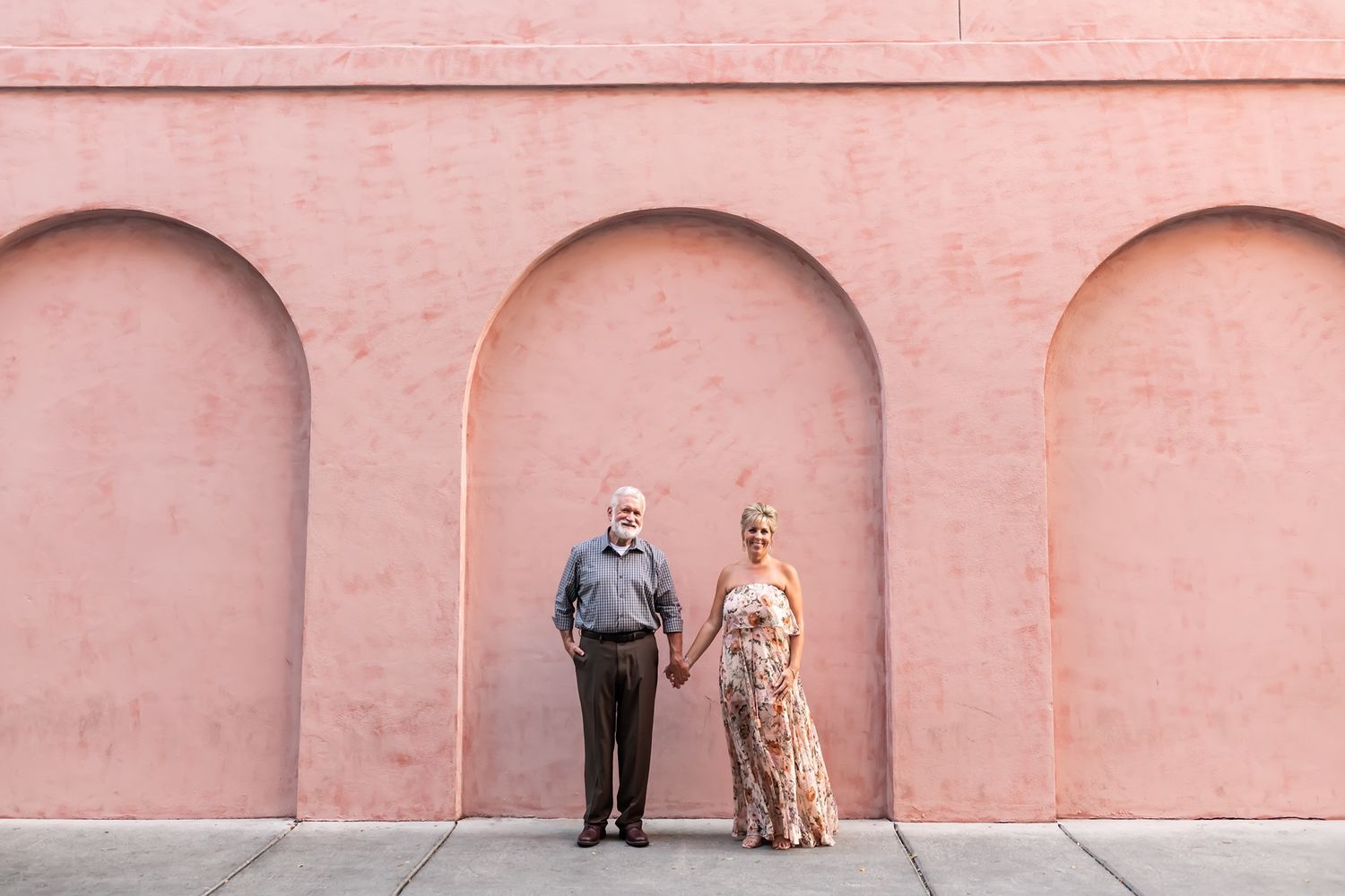 A couple poses together against a pink wall with three arched alcoves.