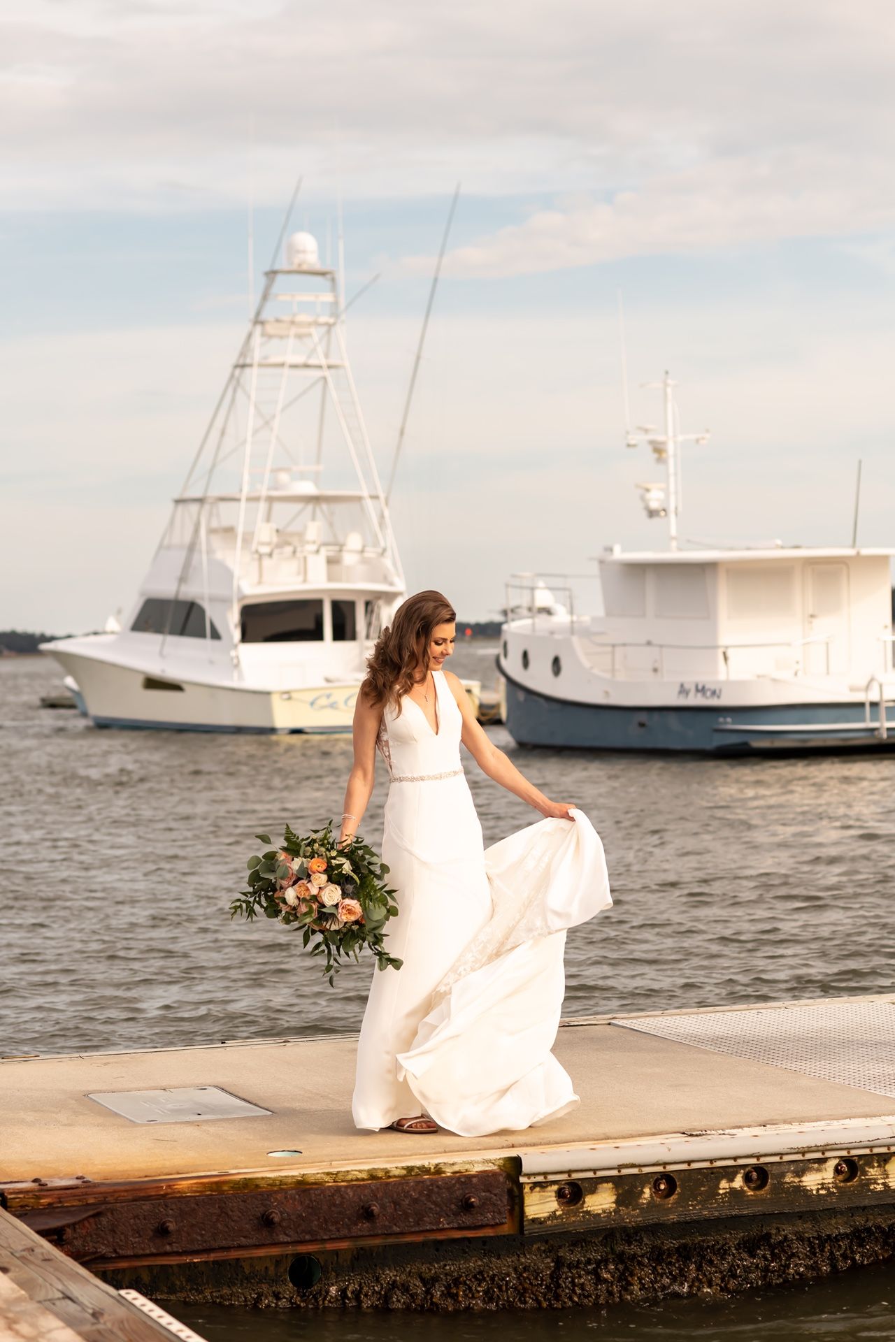 A wedding scene on a marina dock with boats in the background and flowing white dress caught in the sea breeze.
