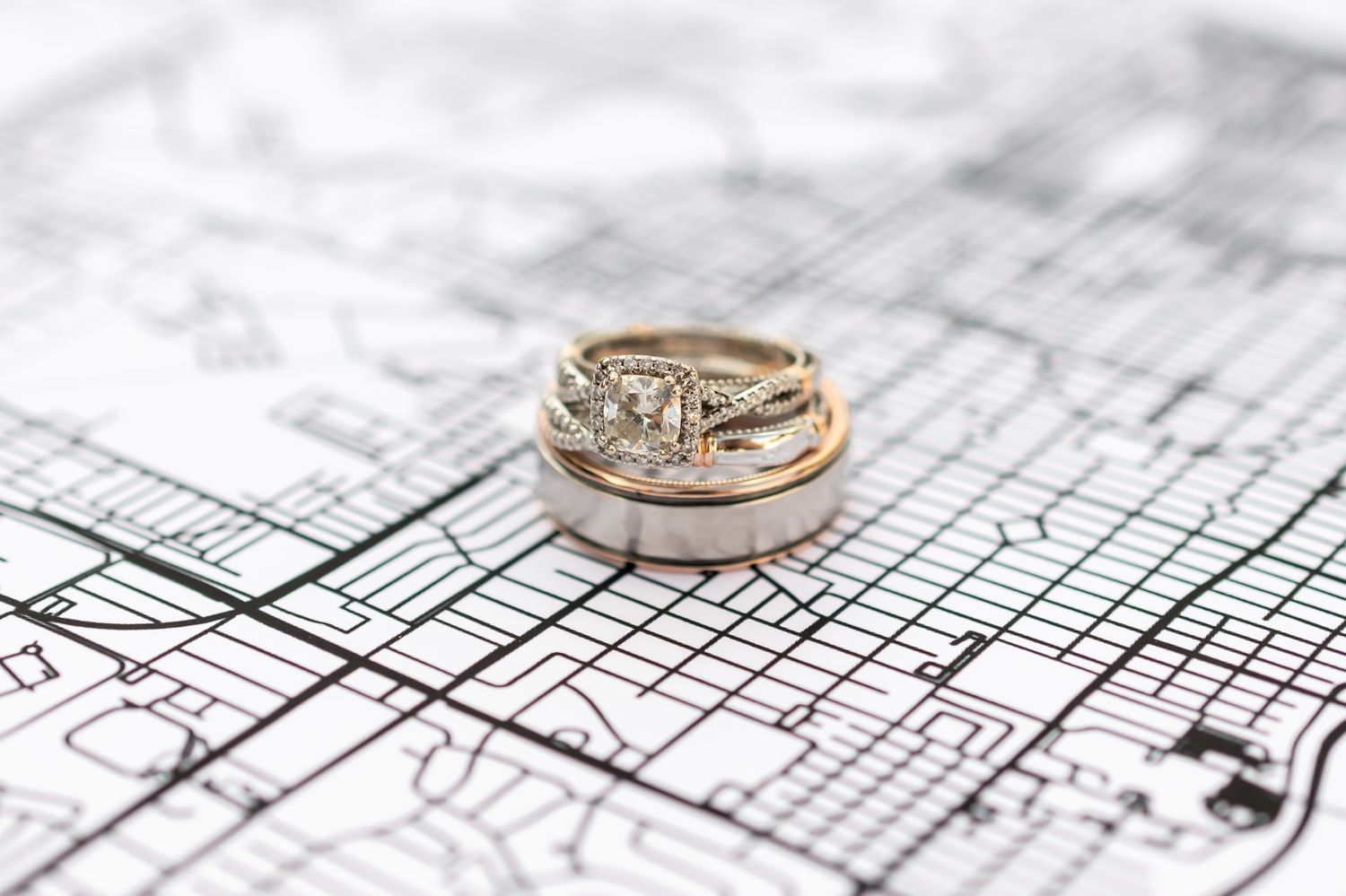 Two wedding rings with diamonds resting on architectural blueprints, symbolizing marriage and building a life together.